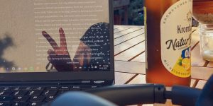 Ein Laptopbildschirm, in dem sich eine Person spiegelt, daneben eine Bierflasche